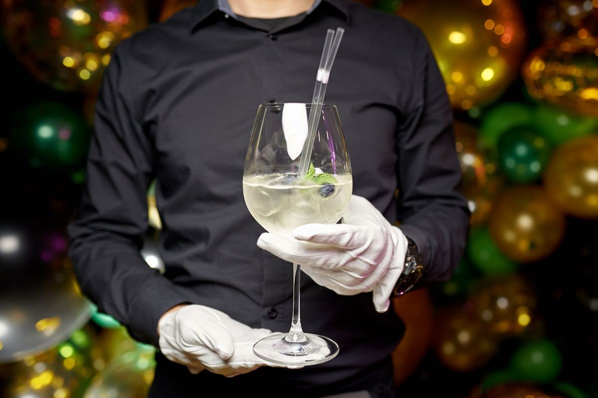 a waiter in white gloves holds a glass of cocktail